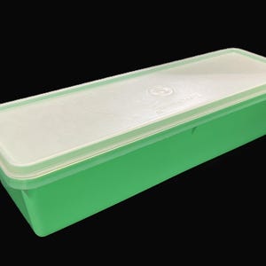 May include: A rectangular, green plastic container with a white lid. The container has a simple, clean design, and the lid fits snugly on top. The container is likely used for storage. The container is made of plastic.