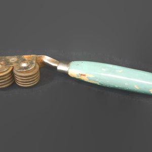 Może przedstawiać: Vintage, drewniany wałek z niebieską, drewnianą rączką i wieloma metalowymi k&oacute;łkami. Wałek jest zardzewiały i ma zużyte wykończenie.