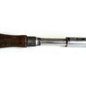 May include: An old-fashioned screwdriver featuring a dark wooden handle and a metal shaft. The handle is a deep brown, and the metal shaft has a silver finish. The screwdriver is designed for manual use and shows signs of wear.