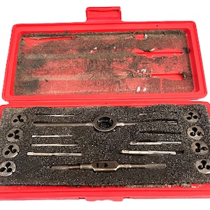 May include: A red toolbox containing a set of metal taps and dies. The tools are arranged in a black foam insert. The toolbox is open, revealing the tools inside. The tools are various sizes and shapes, designed for threading.