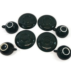 May include: Set of six dark green ceramic teacups and saucers. The cups and saucers have a white rim.