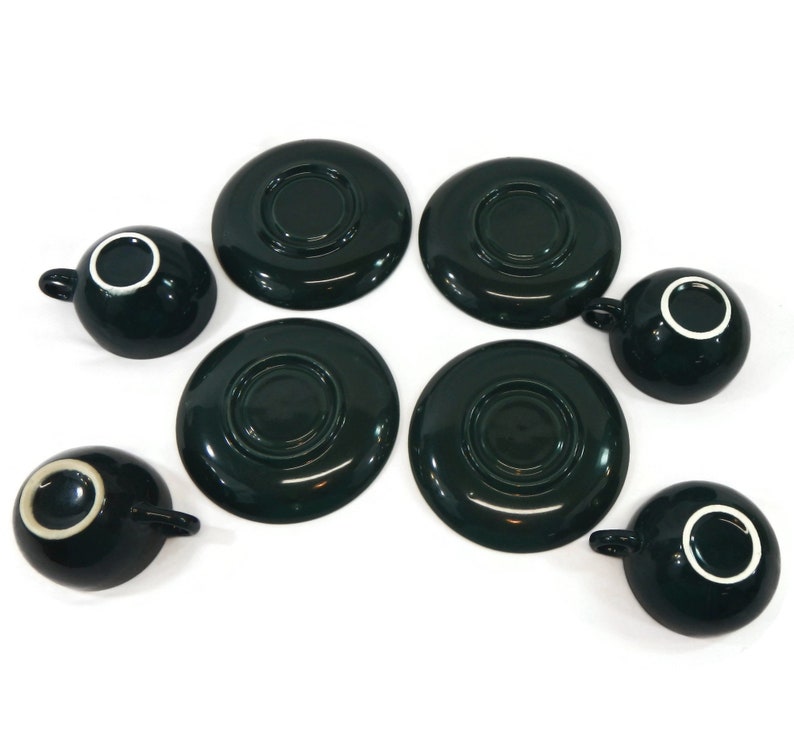 May include: Set of six dark green ceramic teacups and saucers. The cups and saucers have a white rim.