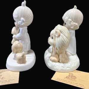 Puede incluir: Dos figuritas de porcelana de ni&ntilde;os, una con un perro y la otra con un le&oacute;n. Las figuritas son blancas con un ligero tono amarillo. La ni&ntilde;a con el perro lleva un perro peque&ntilde;o en brazos. El ni&ntilde;o con el le&oacute;n est&aacute; de pie junto a un le&oacute;n. Las bases de las figuritas son blancas y tienen un ligero tono amarillo. Las bases tienen texto en ellas. El texto en la base de la ni&ntilde;a con el perro dice "Something's Missing When You're Not Around". El texto en la base del ni&ntilde;o con el le&oacute;n dice "And A Child Shall Lead Them A Precious Moments Figurine".