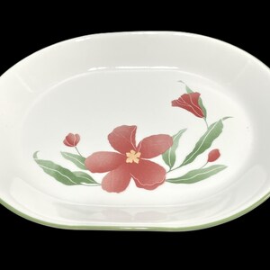 May include: White oval serving dish with a green rim and a floral design featuring red flowers and green leaves.