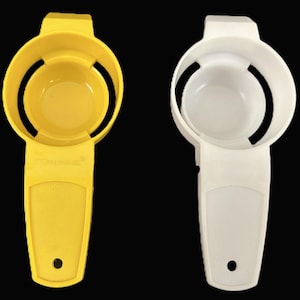 May include: Two plastic egg separators, one yellow and one white, against a black background. Each separator has a handle with a hole, a circular bowl, and a slotted design for separating egg whites from yolks. Kitchen utensil.