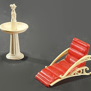 May include: A white plastic dollhouse fountain with a sculpted couple on top and a red plastic chaise lounge with a white frame.