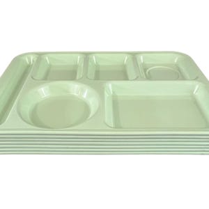 May include: A stack of light green cafeteria trays. Each tray has multiple compartments of various shapes and sizes, including a circular section and several rectangular sections. The trays are made of a durable material.