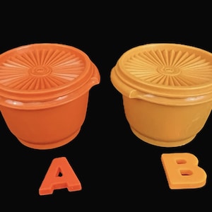 May include: Two vintage orange and yellow Tupperware bowls with matching lids. The lids have a sunburst design. The letters "A" and "B" are below the bowls, indicating the color of each bowl.