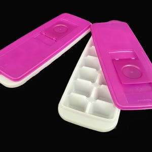 May include: An open ice cube tray in white and fuchsia. The tray has six square compartments. The fuchsia lid is partially open, revealing the tray's interior. The tray is designed for making ice cubes.