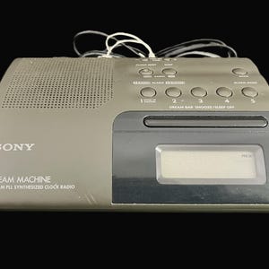 May include: A gray Sony Dream Machine FM/AM PLL synthesized clock radio. The radio has a speaker, buttons for alarm settings, and a digital display. The clock radio has a power cord and antenna.