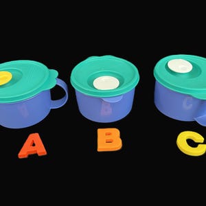 May include: Three blue plastic bowls with teal lids and handles. Each lid has a different coloured centre: yellow, white, and white. Orange, orange, and yellow letters A, B, and C are below the bowls.