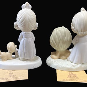 Puede incluir: Dos figuritas de porcelana de personajes de Precious Moments. La figurita de la izquierda presenta a una ni&ntilde;a con un vestido blanco y un perro. La figurita de la derecha presenta a una ni&ntilde;a con un vestido blanco y un le&oacute;n. Ambas figuritas tienen una base blanca con una inscripci&oacute;n amarilla.
