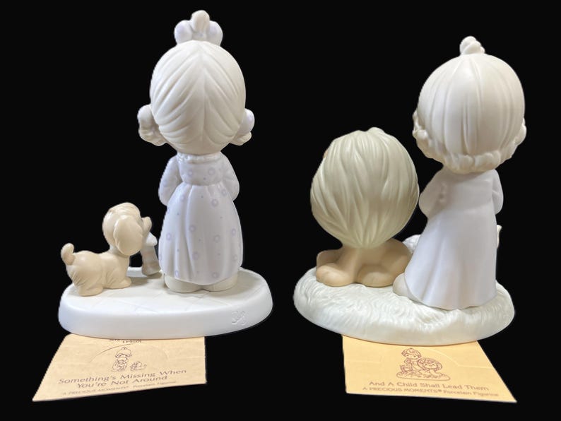 Puede incluir: Dos figuritas de porcelana de personajes de Precious Moments. La figurita de la izquierda presenta a una ni&ntilde;a con un vestido blanco y un perro. La figurita de la derecha presenta a una ni&ntilde;a con un vestido blanco y un le&oacute;n. Ambas figuritas tienen una base blanca con una inscripci&oacute;n amarilla.