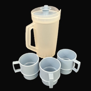 May include: A light beige plastic jug with a lid and handle, alongside three light blue mugs with handles. The jug and mugs are set against a black background. The jug is designed for serving drinks.