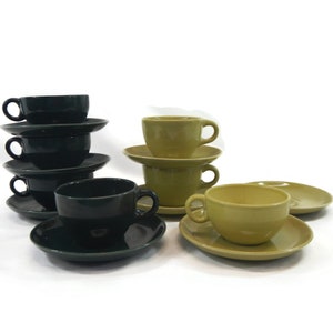 May include: A set of six teacups and saucers, three in dark green and three in a light yellow-green. The cups and saucers are stacked in two separate piles.