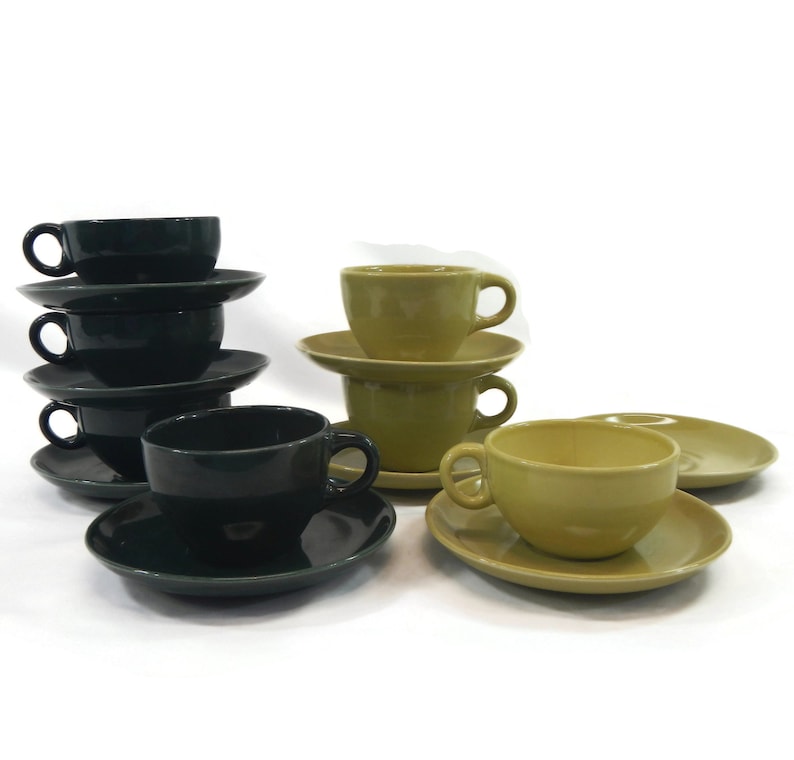 May include: A set of six teacups and saucers, three in dark green and three in a light yellow-green. The cups and saucers are stacked in two separate piles.