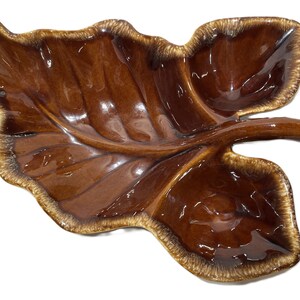 May include: A brown ceramic leaf-shaped serving dish with three sections. The dish has a glossy finish and a light brown rim.