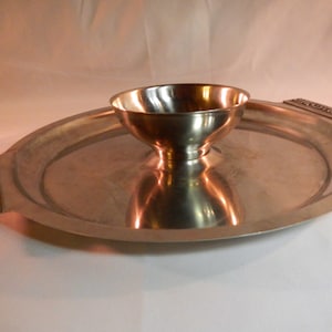 May include: A silver serving tray with a small bowl in the center. The tray has ornate handles on either side.
