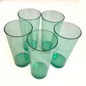 May include: Five clear, green plastic tumblers arranged in a circular pattern. The cups have a slightly tapered design with a solid green base and a clear, transparent body. The rims are smooth and the cups are empty.