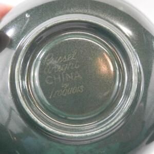 May include: Close-up of the bottom of a green ceramic bowl with the text "Russel Wright China by Iroquois" in white.