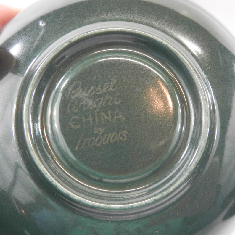 May include: Close-up of the bottom of a green ceramic bowl with the text "Russel Wright China by Iroquois" in white.