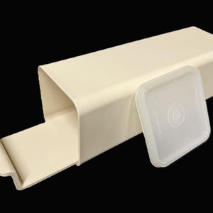 May include: A rectangular, cream-colored plastic storage container with an open end and a sliding tray base. The container includes a separate, translucent, square-shaped plastic lid with a circular embossed design in the center.