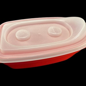 May include: A red plastic food storage container with a clear lid. The lid has two small, round, clear knobs on the top.