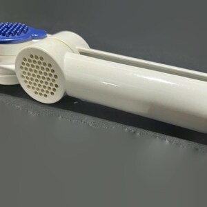 May include: A white and blue garlic press with a long handle and a perforated pressing chamber. The press has a blue, textured surface for pressing garlic cloves. The tool is designed for kitchen use.
