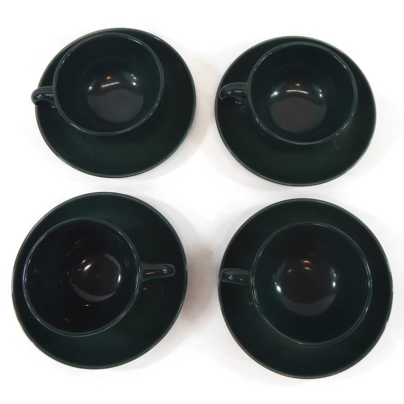 May include: Set of four dark green ceramic teacups and saucers. The cups and saucers are a deep forest green color.