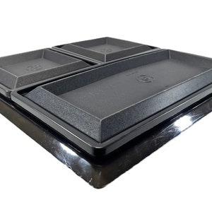 Puede incluir: Cuatro bandejas rectangulares negras con una superficie texturizada, anidadas juntas sobre una base negra.