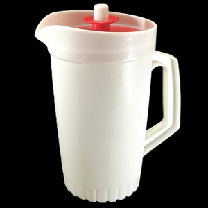 May include: White plastic pitcher with a red lid and a white handle. The pitcher has a textured surface and a ribbed base.