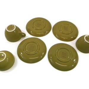 May include: Set of six green teacups and saucers. The cups and saucers are made of ceramic and have a simple, elegant design. The saucers have a slightly raised rim and the cups have a small handle.