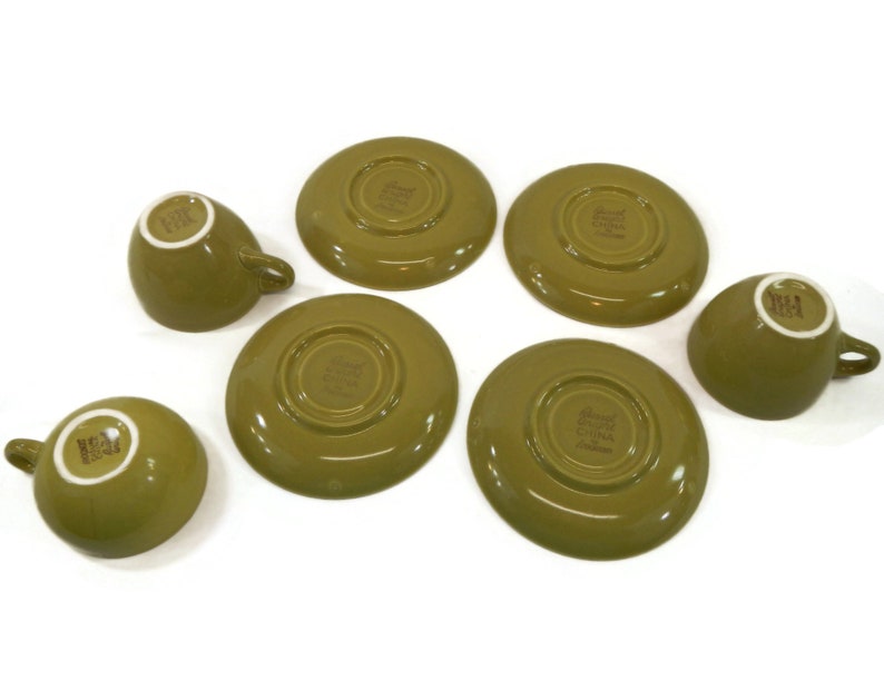 May include: Set of six green teacups and saucers. The cups and saucers are made of ceramic and have a simple, elegant design. The saucers have a slightly raised rim and the cups have a small handle.