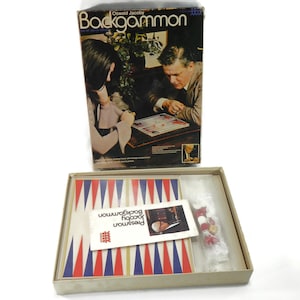 May include: A vintage backgammon game set in a box with a red, white, and blue game board, two sets of checkers, and instructions. The box features a photo of two people playing the game.