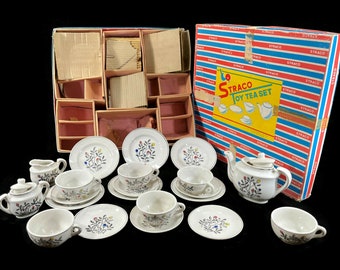 May include: A vintage Straco toy tea set featuring white ceramic pieces with a floral pattern of blue, red, and yellow accents. The set includes a teapot with lid, sugar bowl with lid, creamer, cups, and saucers, all displayed with the original box.