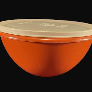 May include: An orange plastic bowl with a cream-colored lid. The bowl has a rounded shape and a smooth surface. The lid fits snugly on top, creating an airtight seal. A classic kitchen storage container.