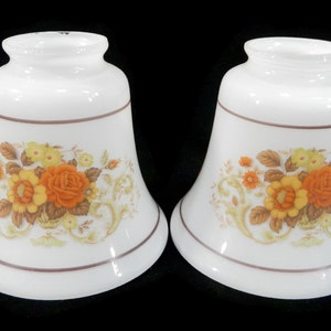 May include: Two white glass lampshades with a floral design. The shades feature a brown, orange, and yellow floral pattern with a brown trim around the top.
