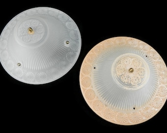 May include: Two white frosted glass ceiling light fixtures with a decorative floral pattern around the edge. The fixture on the left has a plain white edge, while the fixture on the right has a peach-colored edge.