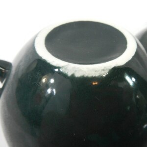 May include: A dark green ceramic teacup with a white rim. The cup is round and has a glossy finish.