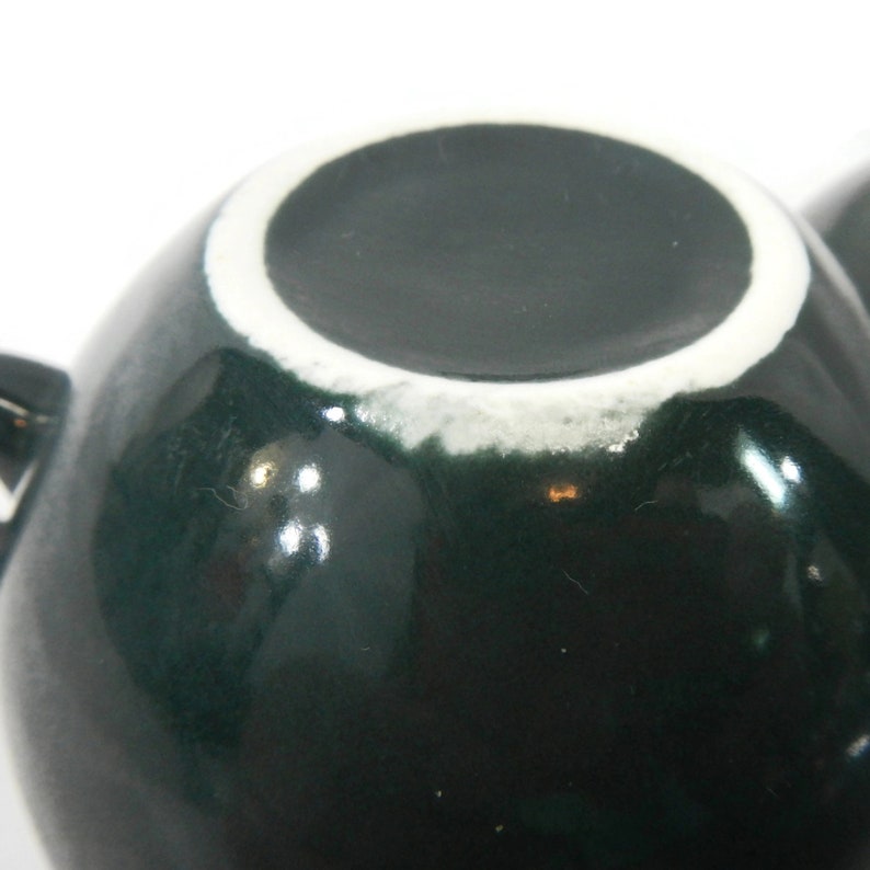 May include: A dark green ceramic teacup with a white rim. The cup is round and has a glossy finish.