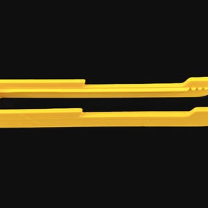 May include: A yellow plastic tool with a U-shaped design. The tool has two parallel arms connected by a curved section. One end of the tool has small teeth. The background is black.