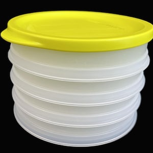 May include: A stackable, clear plastic container with a bright yellow lid. The container has a series of circular, ridged sections, and the lid has a slight lip for easy opening. The background is solid black.