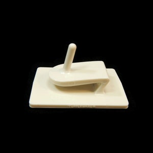 May include: A white plastic hook with an adhesive backing. The hook is designed to be mounted on a wall or other surface. The hook is labeled "Tupperware".