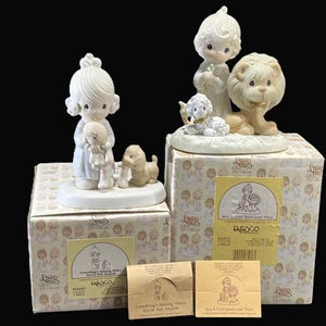 Puede incluir: Dos figuritas Precious Moments con cajas. La primera figurita es una ni&ntilde;a que sostiene una mu&ntilde;eca y un cachorro. La segunda figurita es una ni&ntilde;a con un cordero y un le&oacute;n. Las cajas tienen el logotipo de Precious Moments y los t&iacute;tulos "Something's Missing When You're Not Around" y "And A Child Shall Lead Them There".