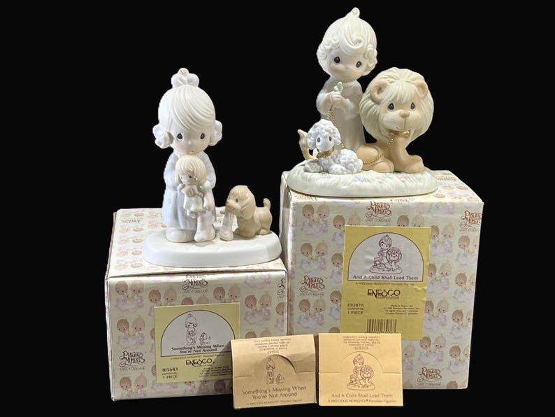 Puede incluir: Dos figuritas Precious Moments con cajas. La primera figurita es una ni&ntilde;a que sostiene una mu&ntilde;eca y un cachorro. La segunda figurita es una ni&ntilde;a con un cordero y un le&oacute;n. Las cajas tienen el logotipo de Precious Moments y los t&iacute;tulos "Something's Missing When You're Not Around" y "And A Child Shall Lead Them There".