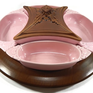 May include: A pink ceramic serving dish with four individual bowls and a lid. The dish is on a wooden base.