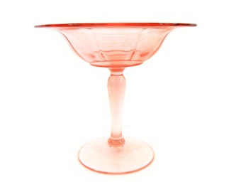 May include: A pink glass pedestal bowl with a fluted rim and a tall, slender stem. The bowl is perfect for serving fruit, candy, or other small treats.