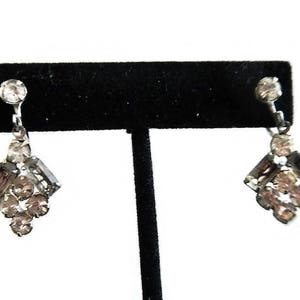 May include: A pair of silver clip-on earrings with a teardrop design. The earrings are adorned with clear and iridescent rhinestones.