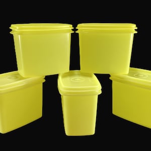 May include: Five yellow plastic food storage containers with matching lids are arranged against a black background. The containers are rectangular with slightly rounded corners. The lids have a raised edge.