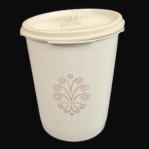 May include: A vintage off-white plastic container with a matching lid. The lid has a radial design. The container features a decorative floral design in a muted mauve color. The container is cylindrical and appears to be a storage item.